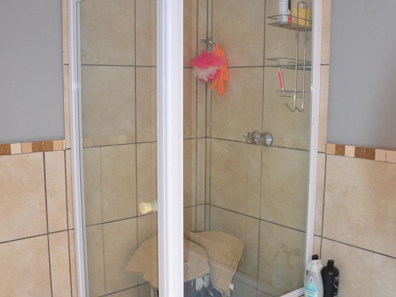 A bathroom featuring a corner shower enclosure with white framing, tiled walls and flooring, and a built-in bathtub.