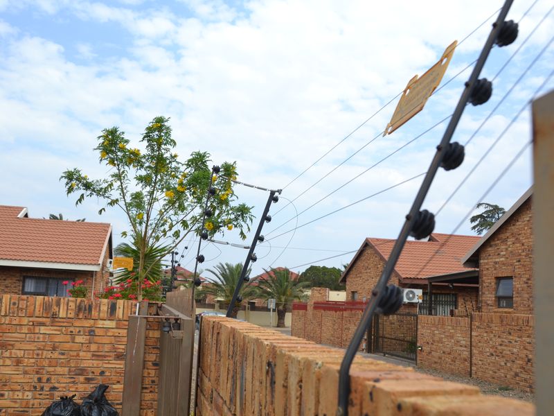 View of the property exterior featuring a face brick boundary wall with installed electric fencing and tiled roof structures in the background.