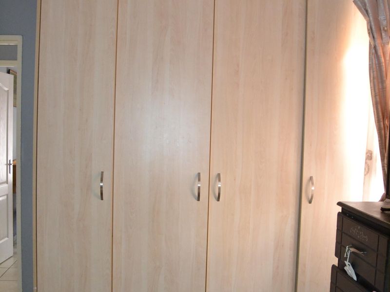 A bedroom featuring a large, light wood-finish built-in wardrobe with modern handles and neutral tiled flooring.