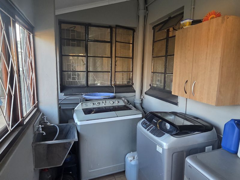 A functional laundry area featuring a metal utility sink, wall-mounted storage cabinetry, and large windows with security bars.