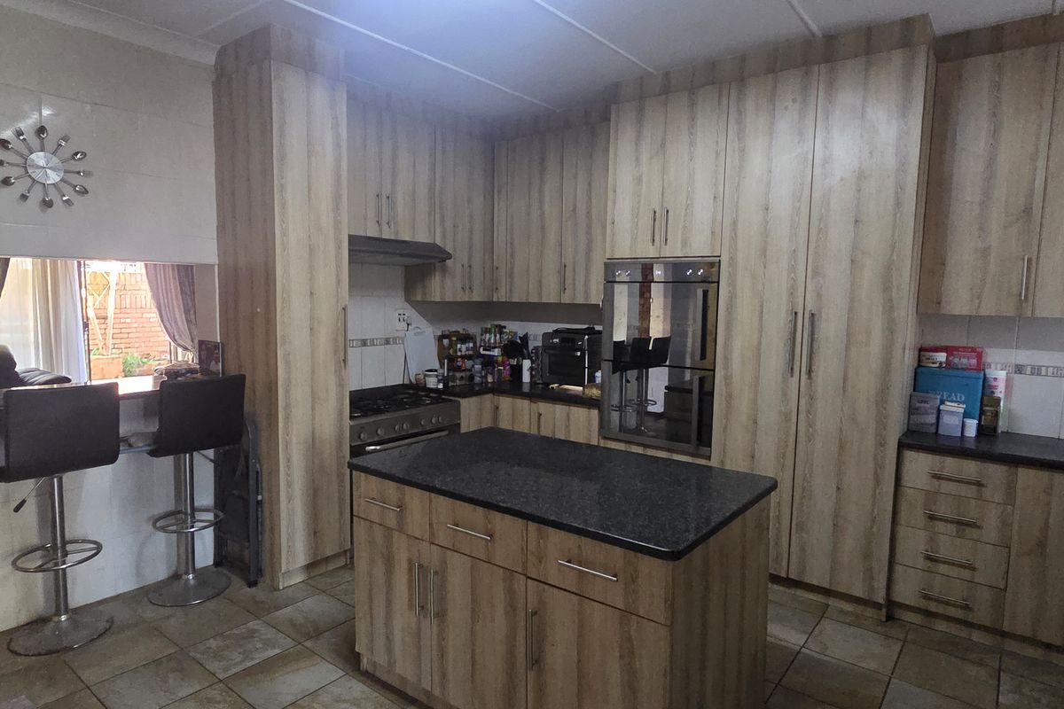 A functional kitchen featuring wood-look cabinetry, a central island with stone countertop, built-in oven, gas hob, and a convenient breakfast bar area.