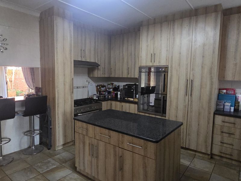 A functional kitchen featuring wood-look cabinetry, a central island with stone countertop, built-in oven, gas hob, and a convenient breakfast bar area.