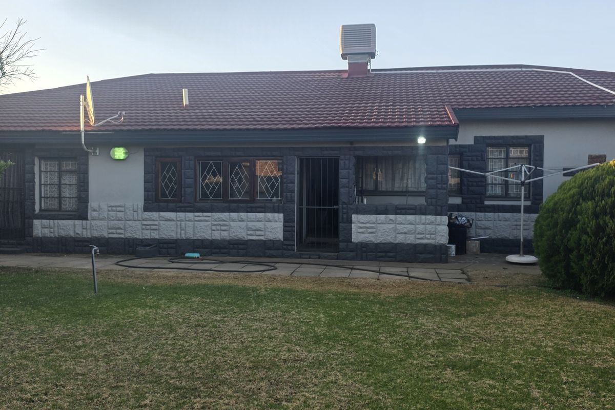 Rear view of the house featuring a tiled roof, stone-clad exterior walls, security gates, and a paved patio area overlooking the garden.