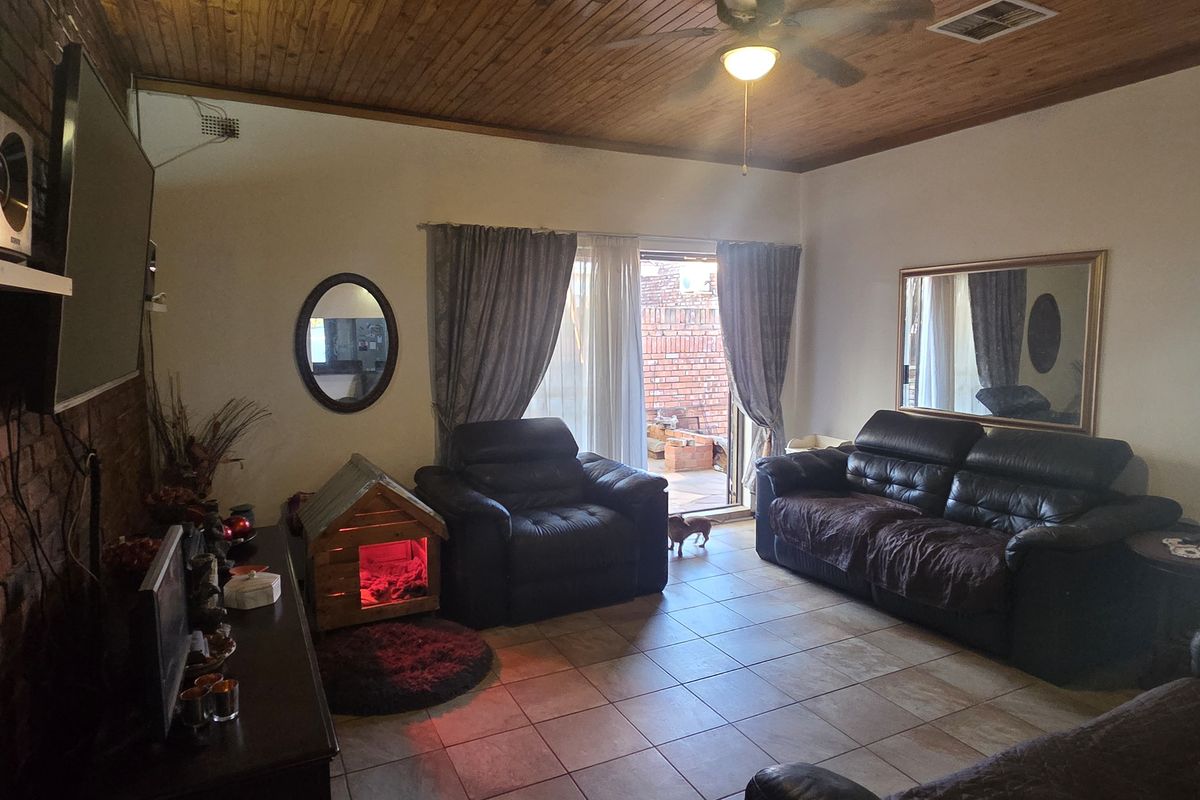 Spacious living room featuring an exposed brick feature wall, timber ceiling, and tiled flooring with direct access to the outdoor area.