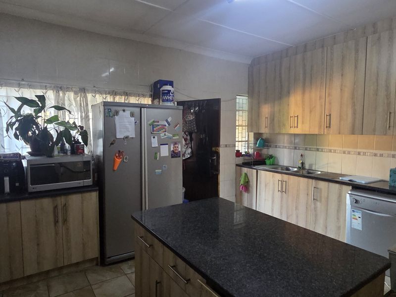 A functional kitchen featuring light wood-look cabinetry, dark granite countertops, a central island, and tiled flooring with ample storage space.