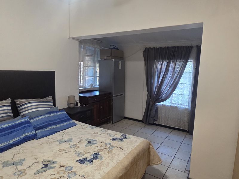 A bedroom featuring built-in cupboards and tiled flooring, offering a functional layout with an adjoining space.