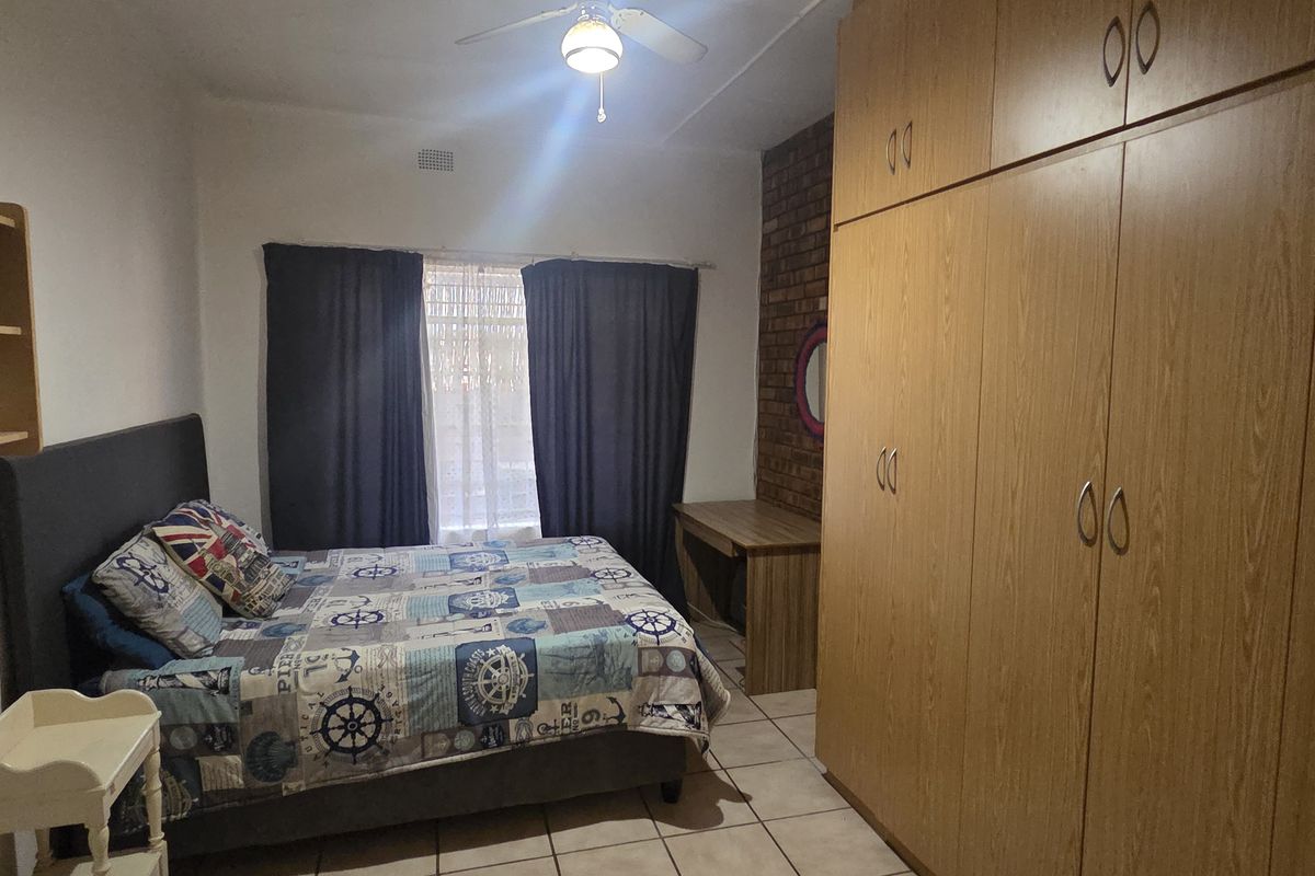 A bedroom featuring built-in wooden cupboards, an exposed brick feature wall, tiled flooring, and a ceiling fan.