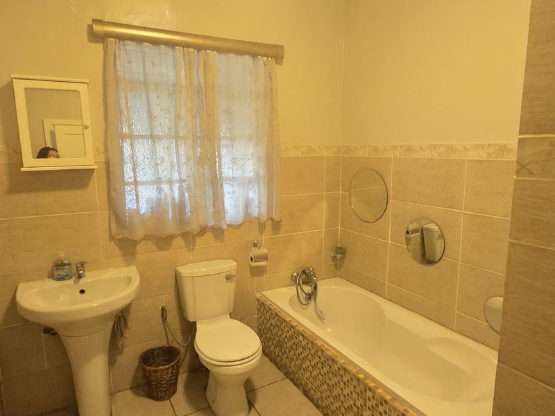 A functional bathroom featuring a pedestal basin, toilet, and bathtub with neutral wall and floor tiling.