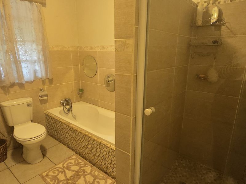 A functional bathroom featuring a pedestal basin, toilet, built-in bathtub, and a separate glass-enclosed shower with tiled finishes throughout.