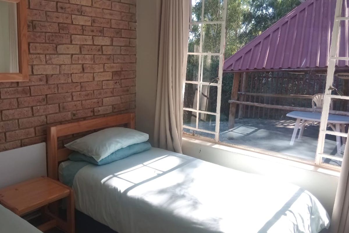 A bedroom featuring an exposed brick feature wall and a large window providing natural light and views of the outdoor patio area.