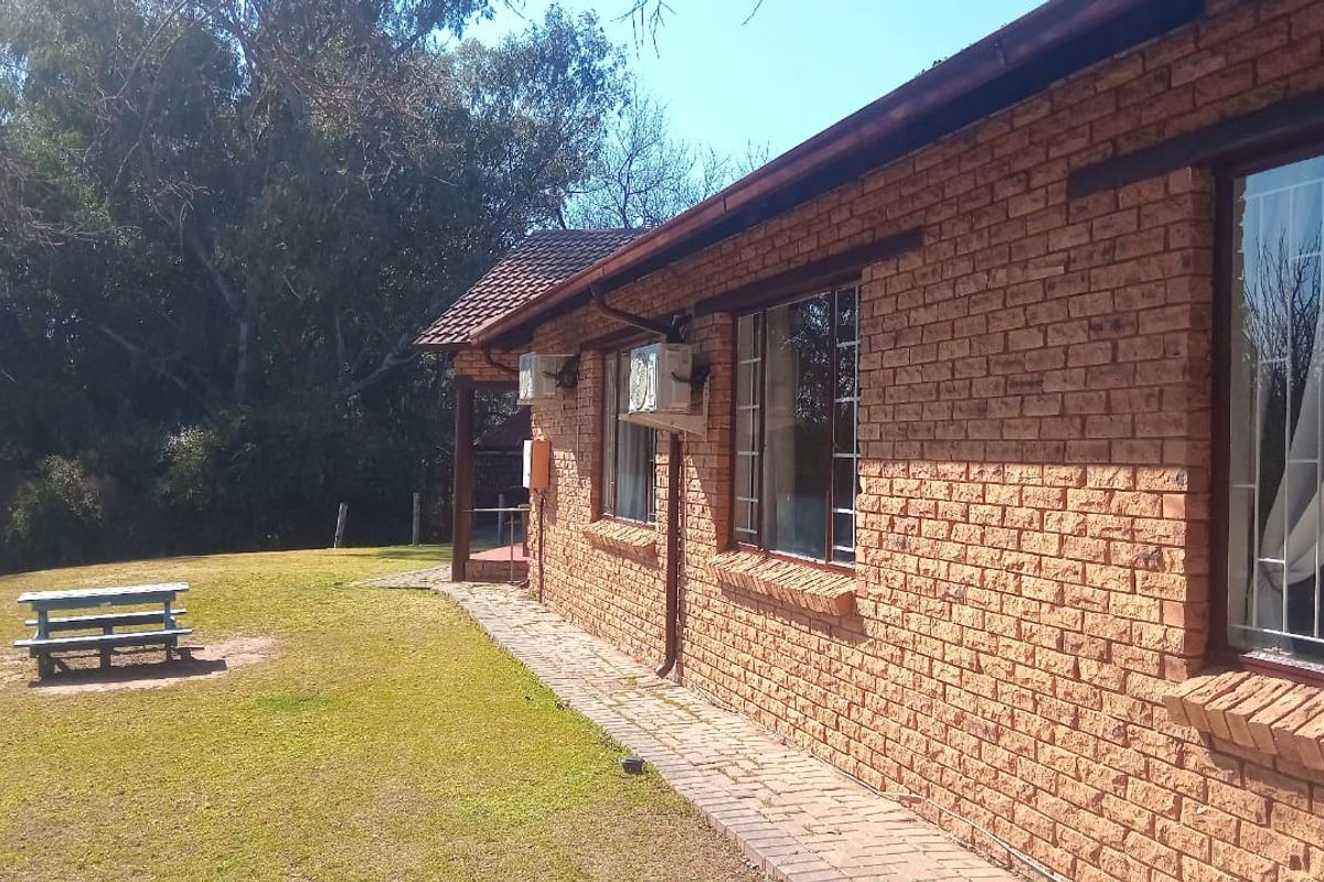 Rear view of a face-brick dwelling featuring a paved walkway, aluminium window frames with security bars, and an external air conditioning unit.