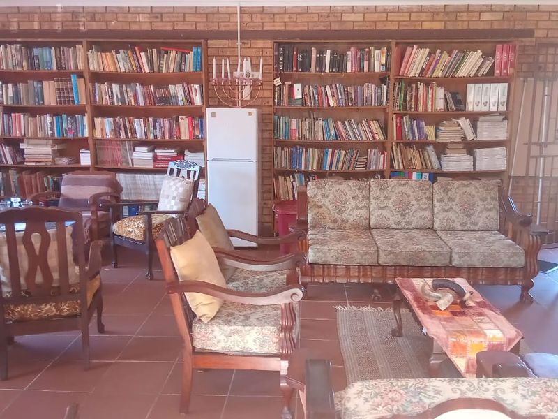 Spacious living area featuring extensive built-in wooden bookshelves, exposed brick walls, and durable tiled flooring, offering a rustic and functional space.