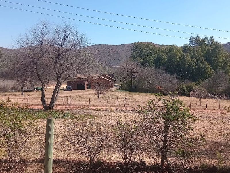 A wide-angle view of the small holding property featuring open land, wire fencing, and the main dwelling structure set against a mountain backdrop.