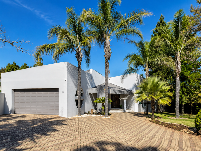 Modern front facade featuring a paved driveway, double garage, and a covered entrance surrounded by established palm trees and landscaped garden.