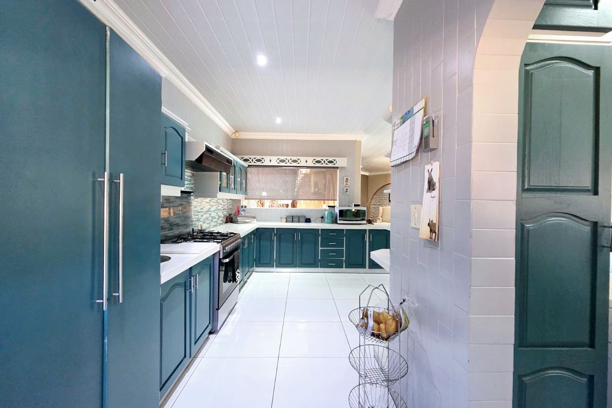 A well-maintained kitchen featuring teal cabinetry, gas stove with extractor, tiled flooring, and a classic tongue and groove ceiling.