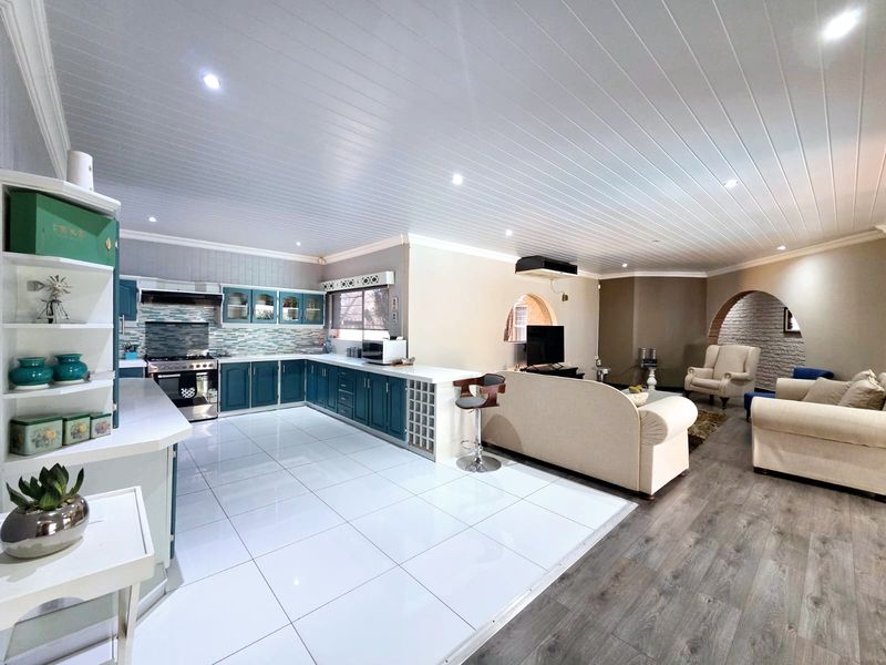 Spacious open-plan living area featuring a modern kitchen with blue cabinetry, tiled and laminate flooring, and elegant architectural archways.