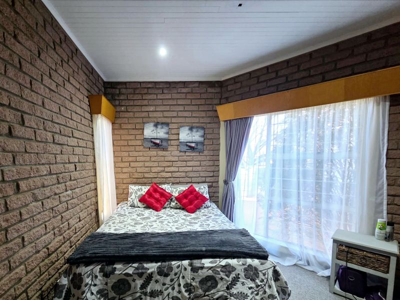 A cozy bedroom featuring rustic exposed brick walls, timber window pelmets, and large windows allowing for natural light.