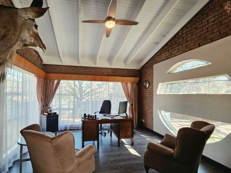 A well-lit home office featuring exposed brick walls, a vaulted ceiling with exposed beams, and unique circular feature windows.