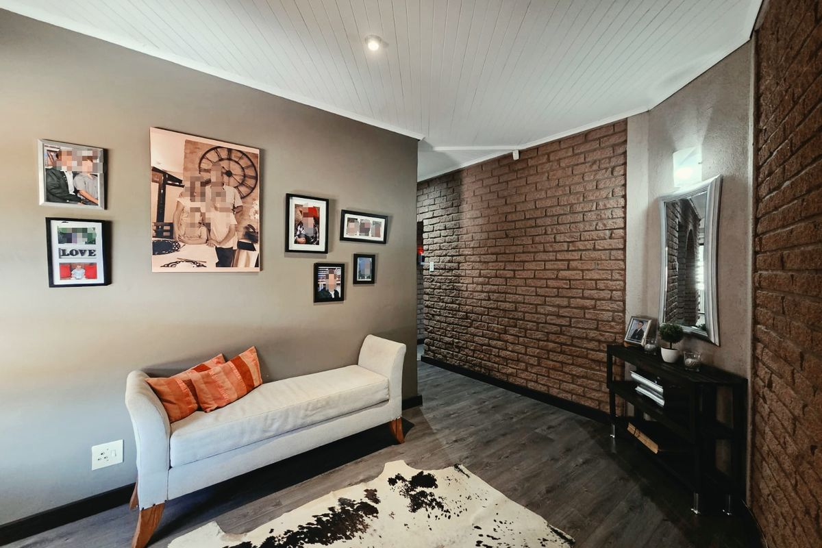 A living area featuring a textured exposed brick feature wall, modern laminate flooring, and a white tongue and groove ceiling with recessed lighting.