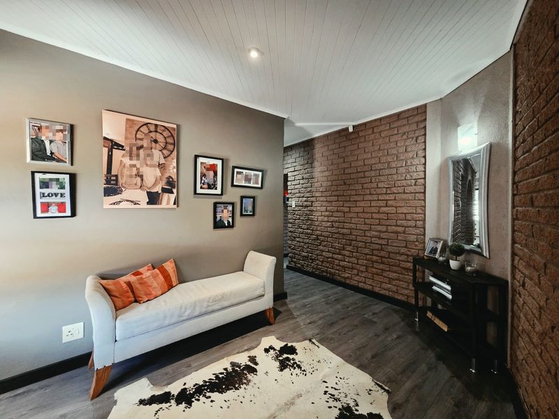 A living area featuring a textured exposed brick feature wall, modern laminate flooring, and a white tongue and groove ceiling with recessed lighting.