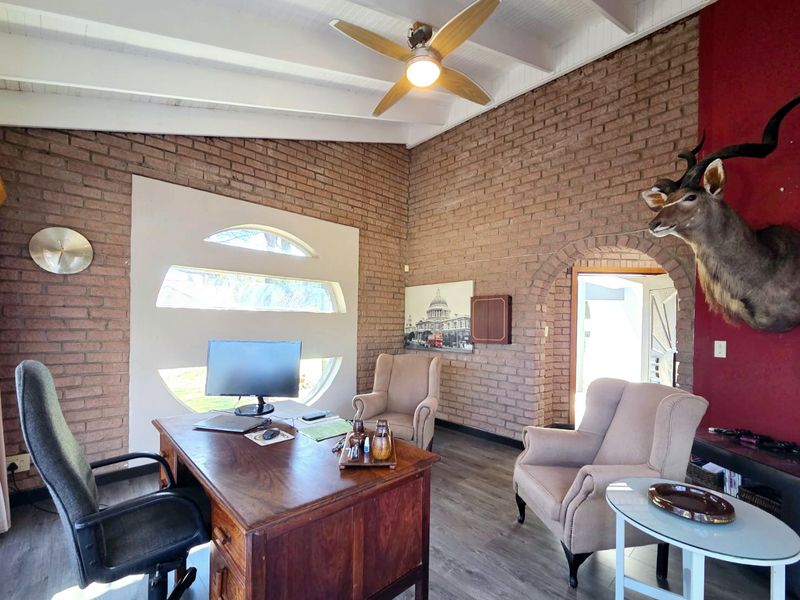 A spacious home office featuring exposed brick walls, a vaulted ceiling with a fan, and a unique arched window design.