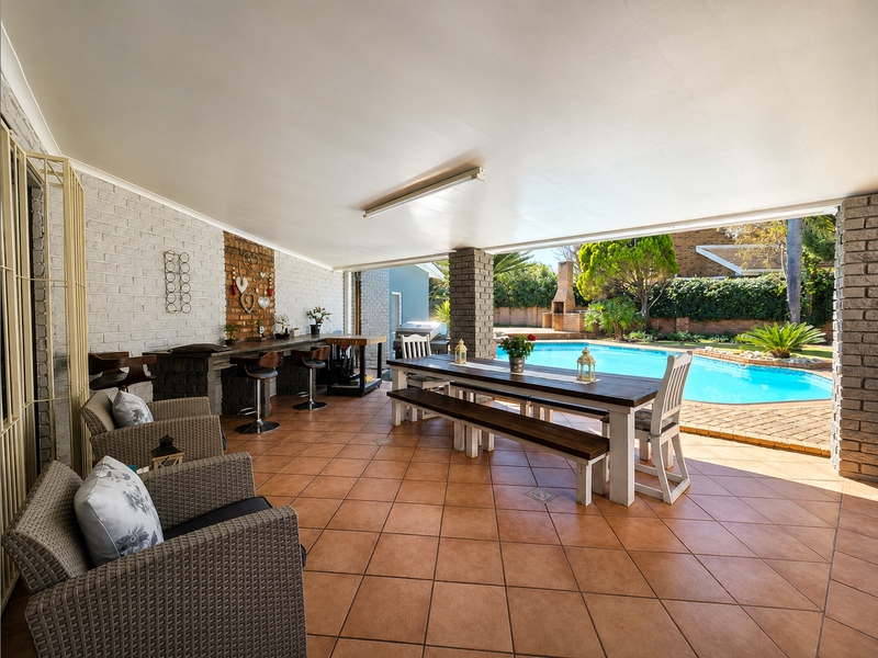 Spacious covered patio featuring a built-in brick bar, tiled flooring, and direct access to the swimming pool area, perfect for outdoor entertaining.