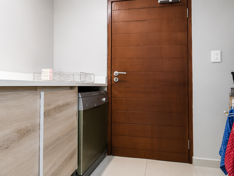 A functional laundry area featuring light wood-finish cabinetry, a modern sink, and a built-in dishwasher, complemented by a solid timber door.