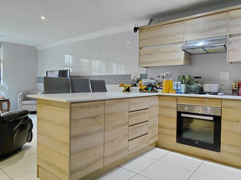 Modern open-plan kitchen and living area featuring light wood-finish cabinetry, integrated appliances, and neutral tiled flooring throughout.