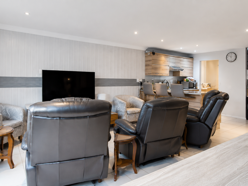 Spacious open-plan living area featuring tiled floors, recessed lighting, a modern kitchen with breakfast counter, and an integrated staircase.