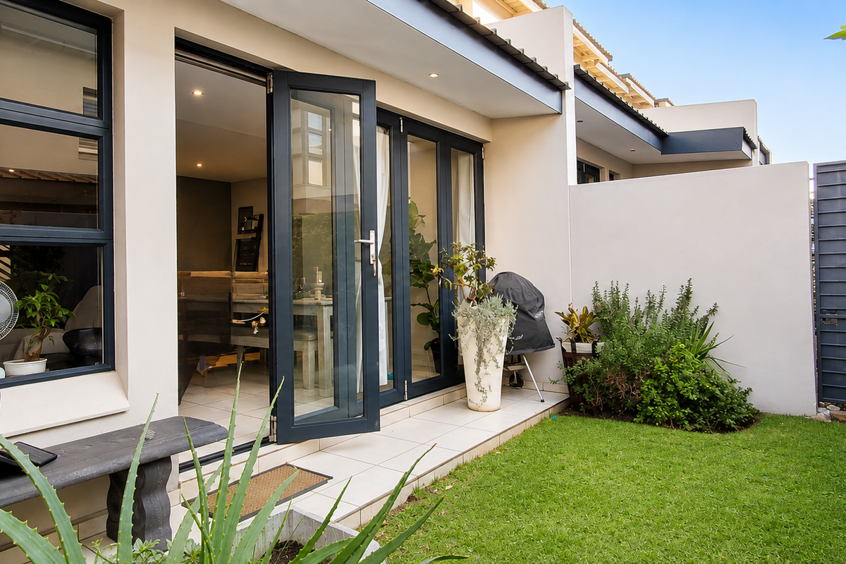 A well-maintained rear townhouse garden featuring a tiled patio, modern aluminium stacker doors, and a private lawn area.
