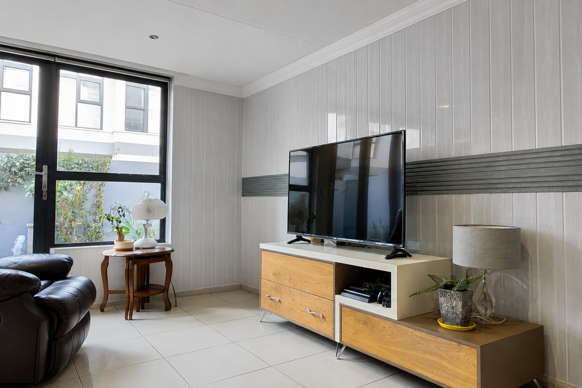 A bright living room featuring modern tiled flooring, decorative wall paneling, and a large glass sliding door providing natural light and access to the exterior.