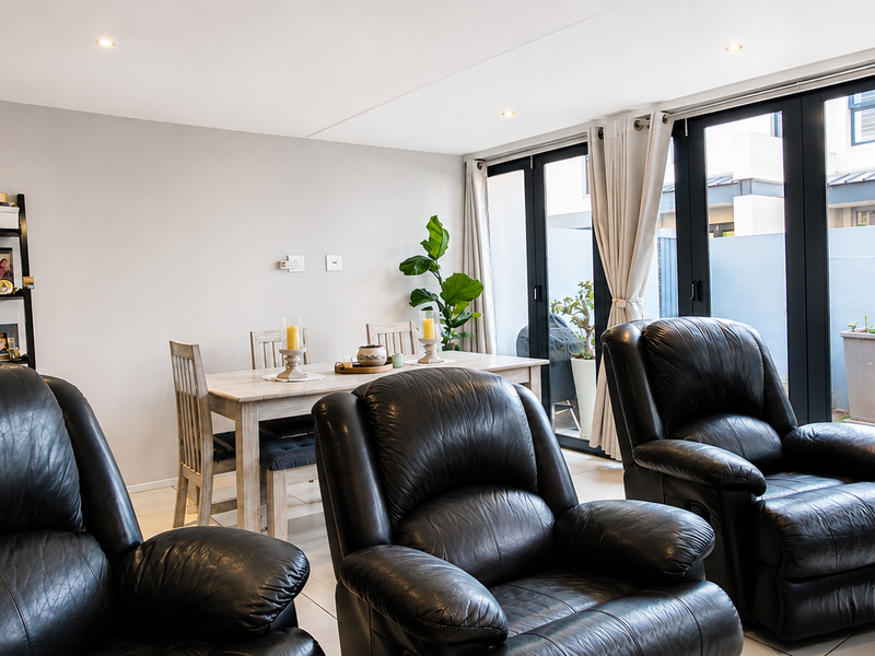 Bright open-plan living and dining area featuring modern tiled floors, recessed lighting, and large black aluminium folding doors leading to an outdoor space.