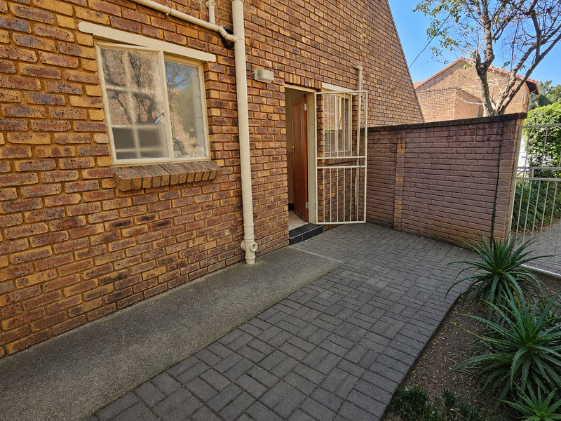 A private paved rear courtyard featuring face brick walls, secure access gate, and security bars on windows and doors.