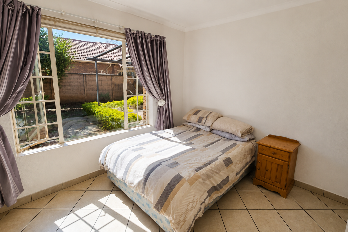 A bright bedroom featuring tiled flooring and a large window overlooking the rear garden area.