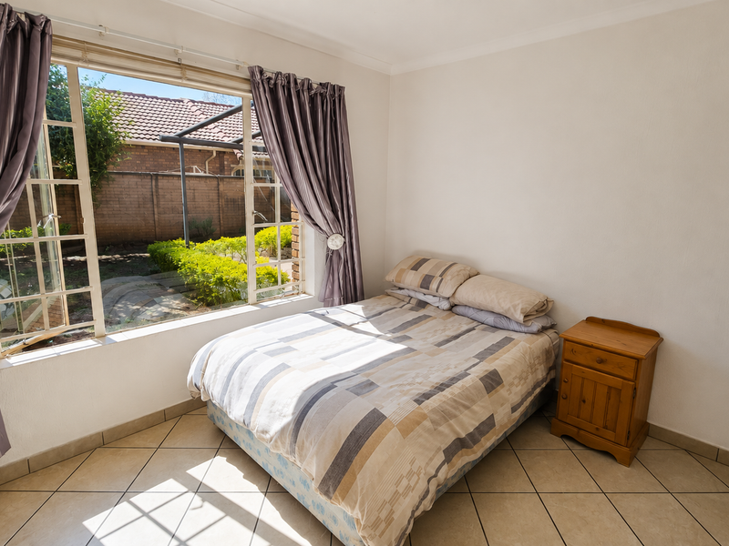 A bright bedroom featuring tiled flooring and a large window overlooking the rear garden area.