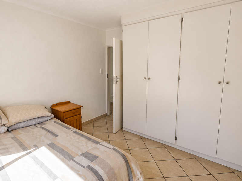 A bedroom featuring neutral tiled flooring and ample built-in cupboard storage space.