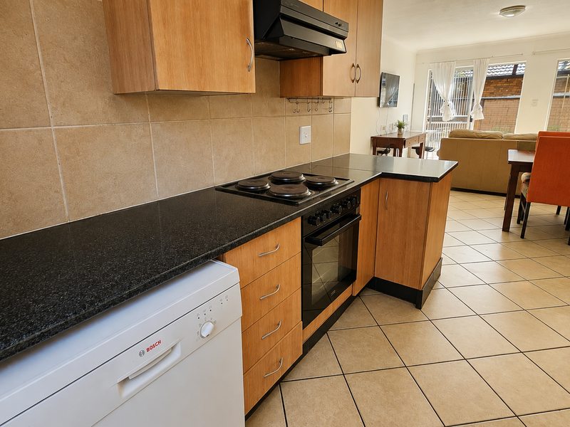 Open-plan kitchen featuring laminate cabinetry, granite countertops, and built-in appliances, flowing into a dining and living area with tiled flooring throughout.