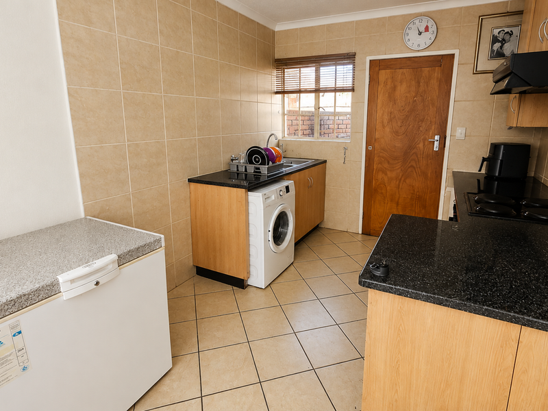 Functional kitchen featuring light wood cabinetry, dark countertops, ceramic tile backsplash, and integrated electric hob with extractor fan.