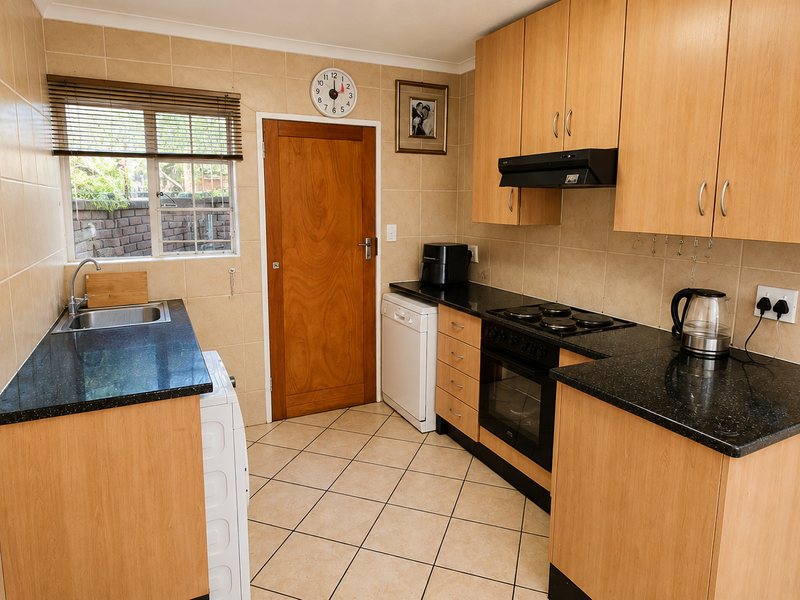 A functional kitchen featuring laminate cabinetry, granite countertops, built-in oven with hob, and tiled finishes throughout.