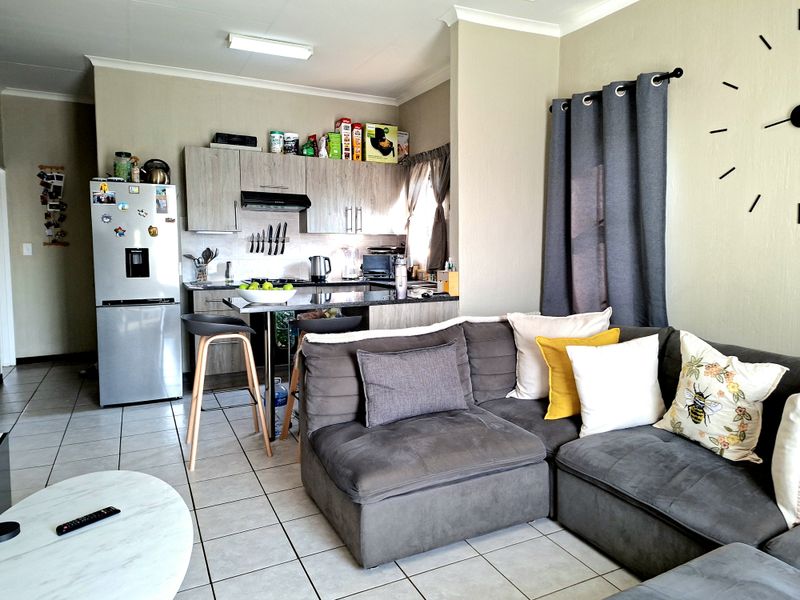 Open-plan living area featuring a compact kitchen with built-in cabinetry, a breakfast counter, and tiled flooring throughout the combined space.