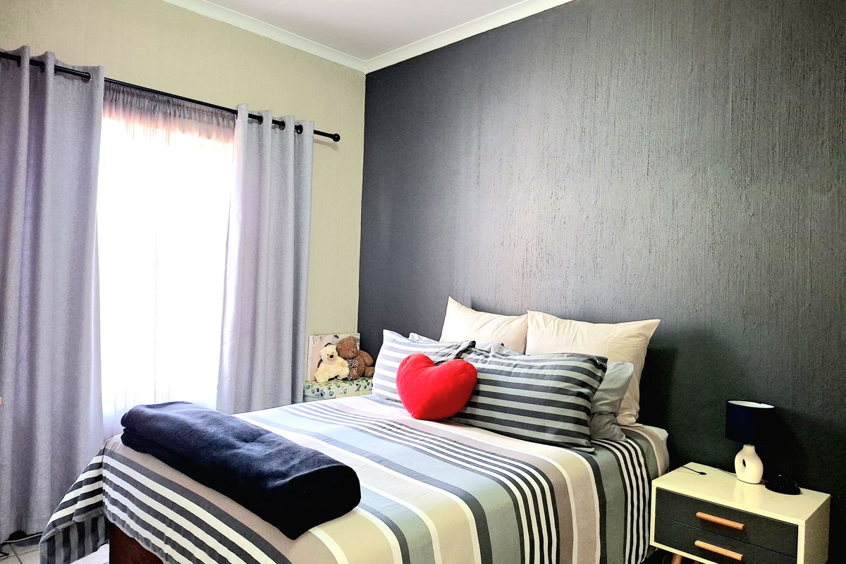 A well-maintained bedroom featuring a dark textured accent wall, neutral wall tones, and a large window with curtain tracks.