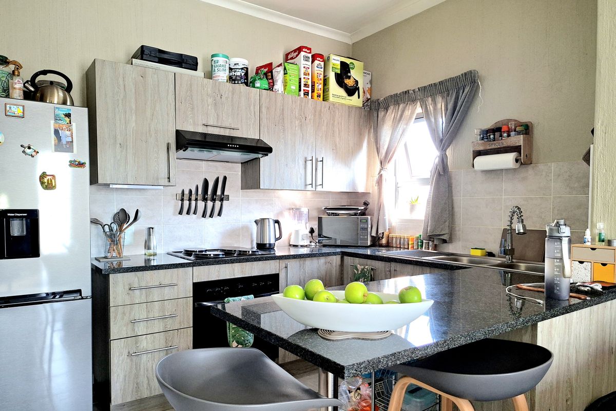A functional kitchen featuring modern laminate cabinetry, granite countertops, a built-in oven with extractor fan, and a double sink with a tiled backsplash.