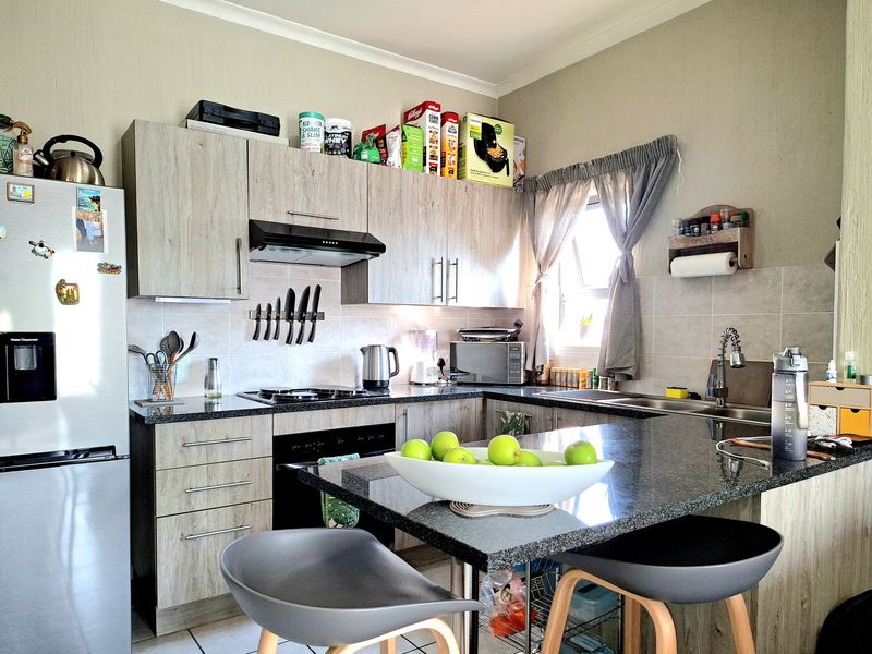 A functional kitchen featuring modern laminate cabinetry, granite countertops, a built-in oven with extractor fan, and a double sink with a tiled backsplash.
