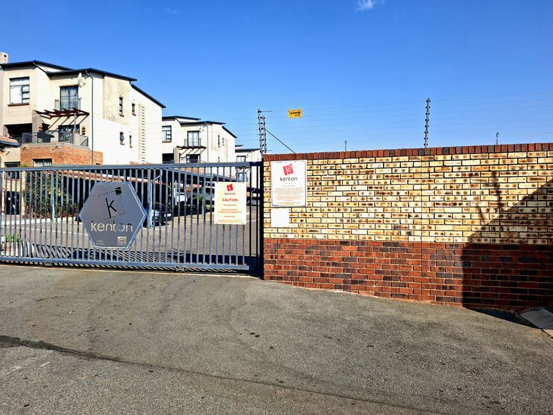 Secure gated entrance to the apartment complex featuring a brick boundary wall, electric fencing, and a sliding vehicle access gate.