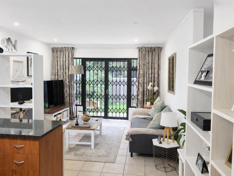 Bright open-plan living area featuring tiled floors, recessed lighting, and sliding glass doors with security gates leading to the outdoor space.