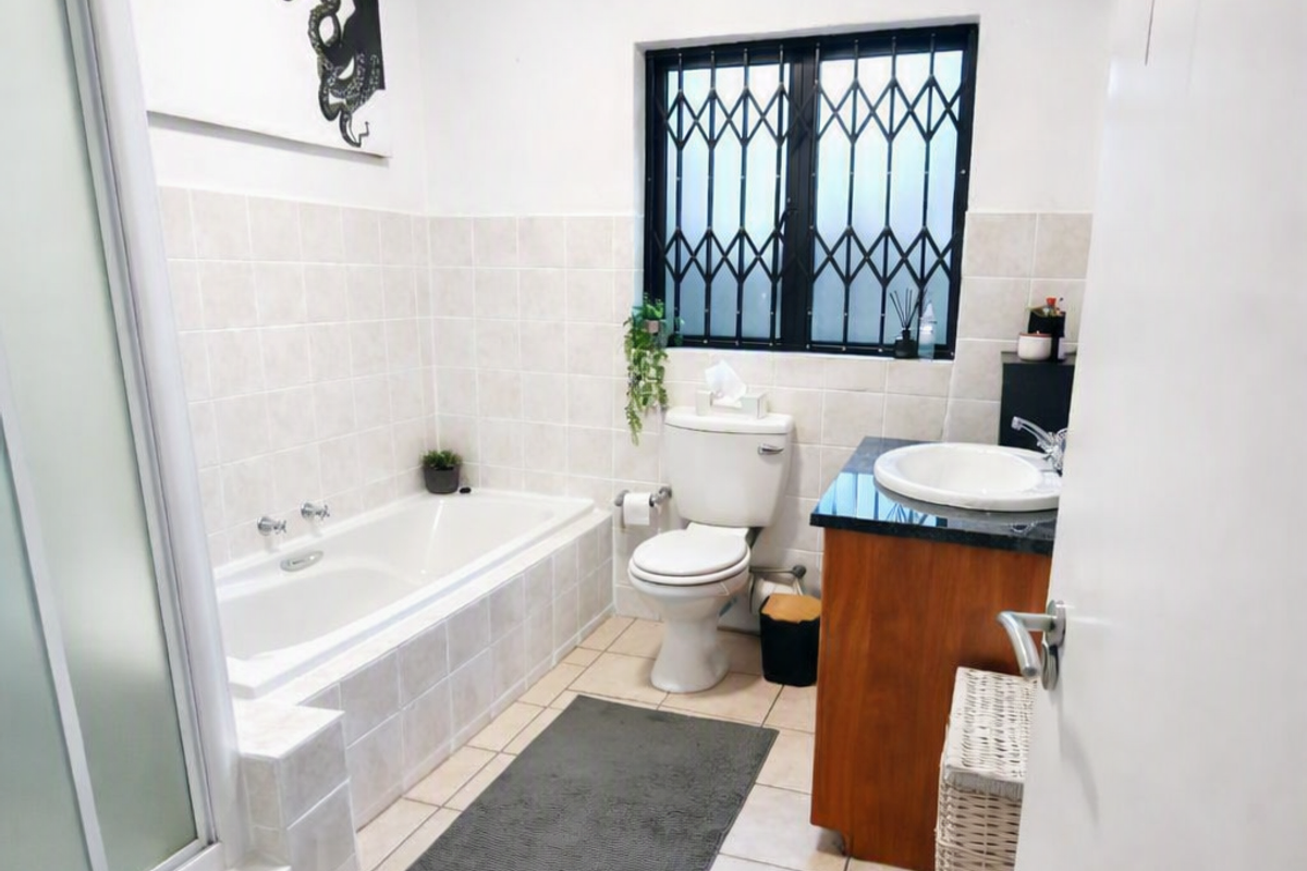 A functional bathroom featuring a built-in bathtub, separate shower enclosure, vanity with basin, and tiled finishes throughout.