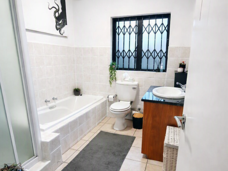 A functional bathroom featuring a built-in bathtub, separate shower enclosure, vanity with basin, and tiled finishes throughout.