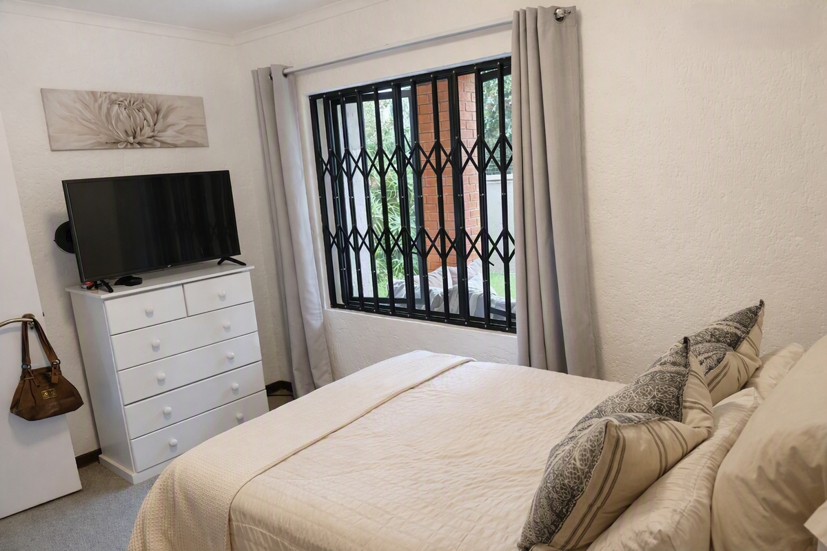 A well-maintained bedroom featuring neutral walls, carpeted flooring, and a window fitted with a black security gate.