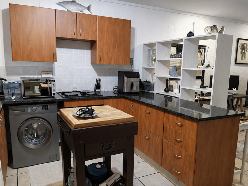 A functional kitchen featuring wood-look laminate cabinetry, dark granite countertops, a tiled backsplash, and integrated space for laundry appliances.