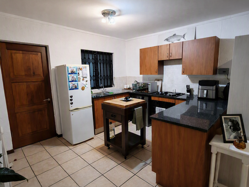 Functional kitchen featuring granite countertops, wooden cabinetry, tiled flooring, and integrated cooking appliances, offering a practical layout for daily meal preparation.